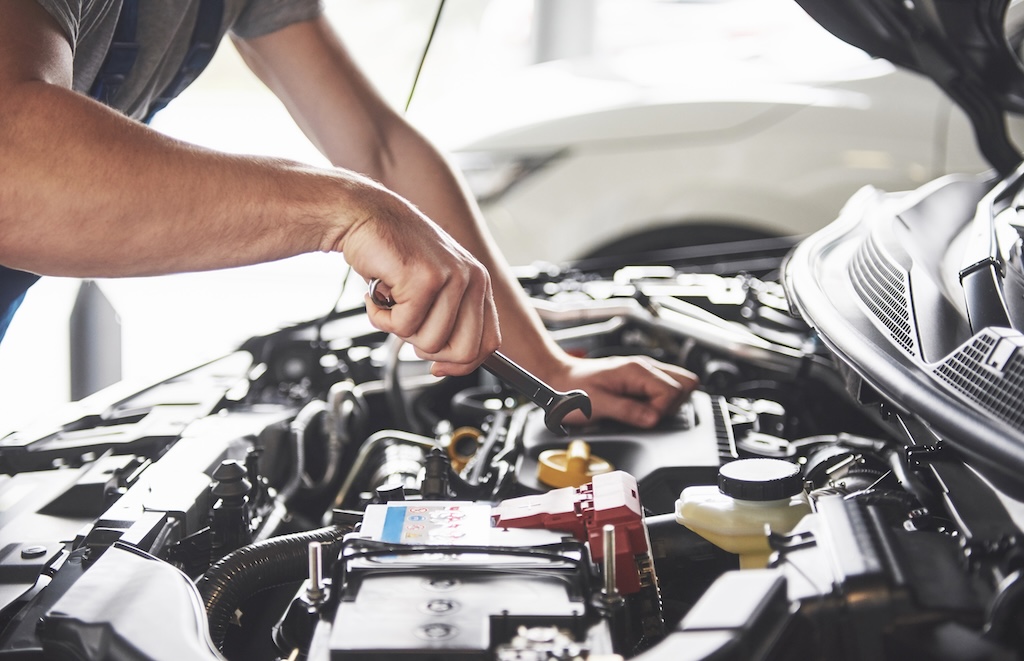 car service worker repairing vehicle with wrench.