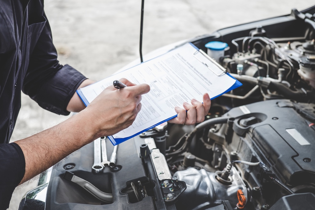 Automobile mechanic repairman checking a car engine with inspecting writing to the clipboard the checklist for repair machine, Mercedes service A vs B